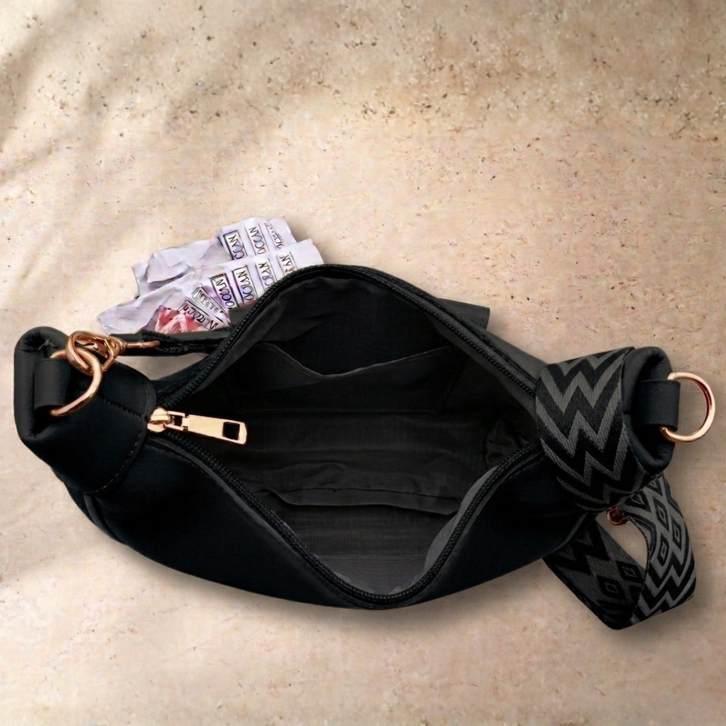 Black waist bag with a patterned strap on a beige surface