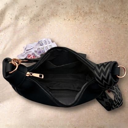 Black waist bag with a patterned strap on a beige surface