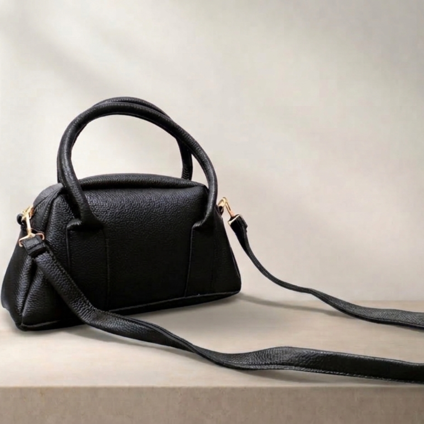 Black handbag with a strap on a light gray background