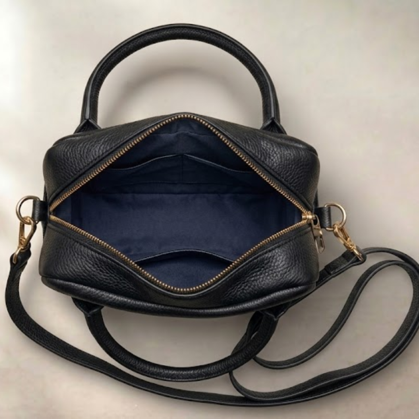 Black leather handbag with a strap on a light beige background