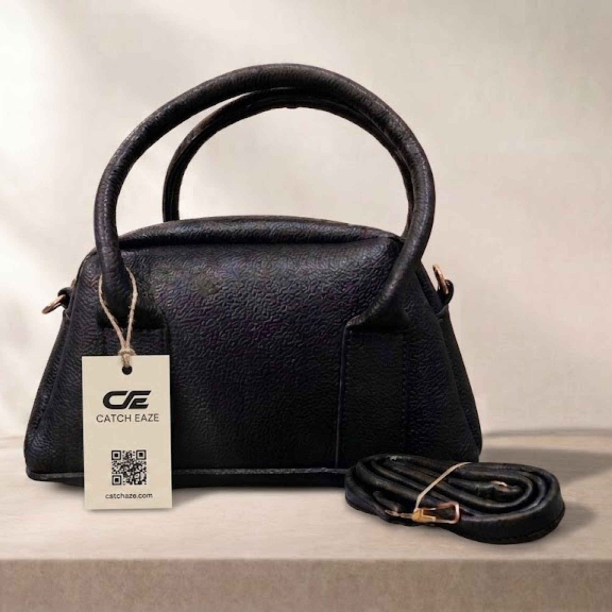 Black handbag with a matching strap on a light background, featuring a 'Catch Eaze' tag.