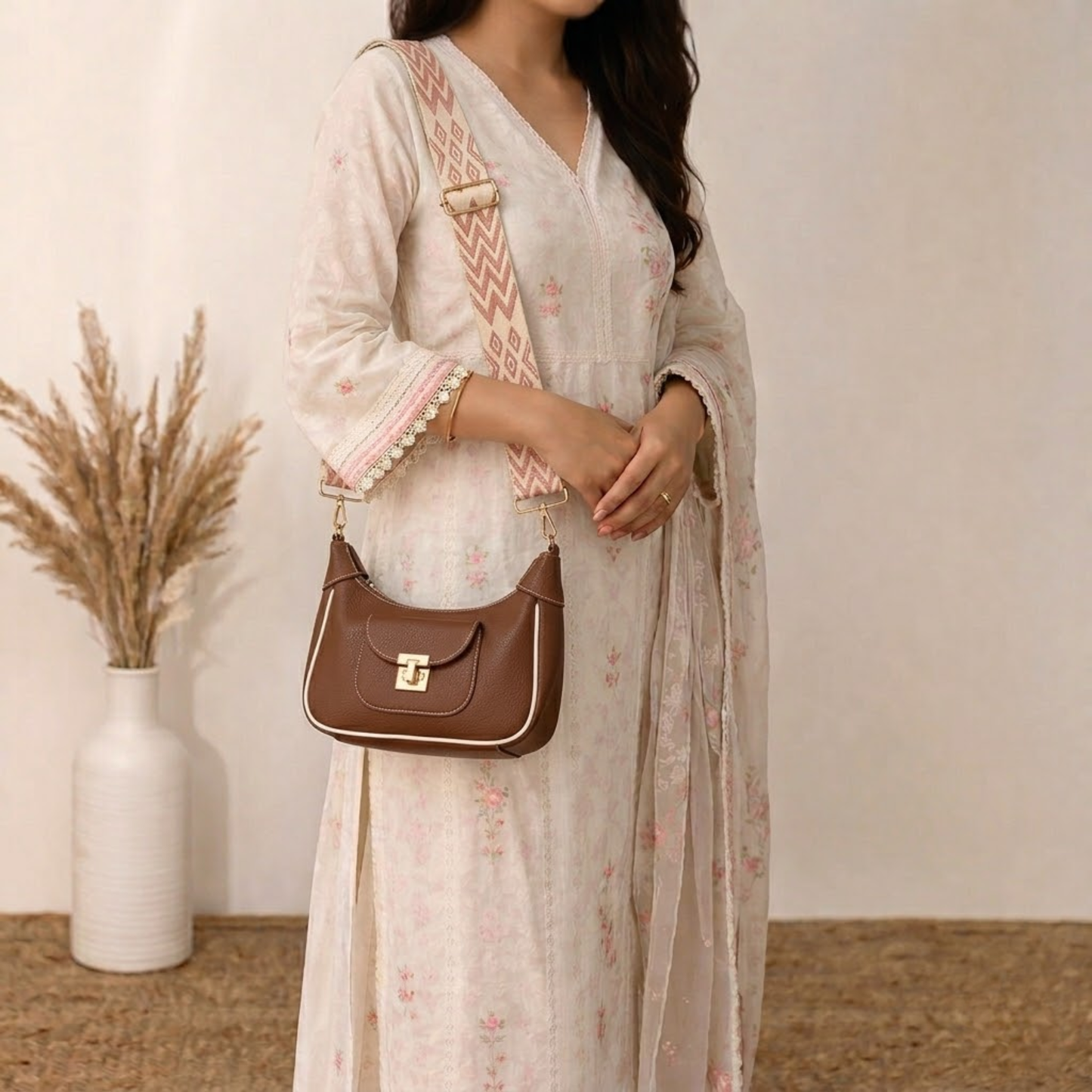 Woman holding a brown handbag wearing a light-colored traditional outfit with a neutral background