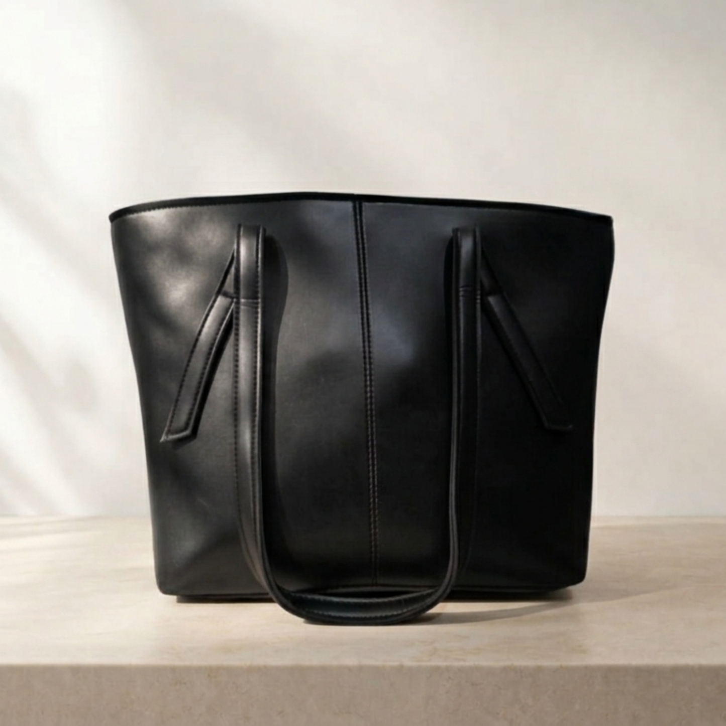 Black leather tote bag on a light beige background