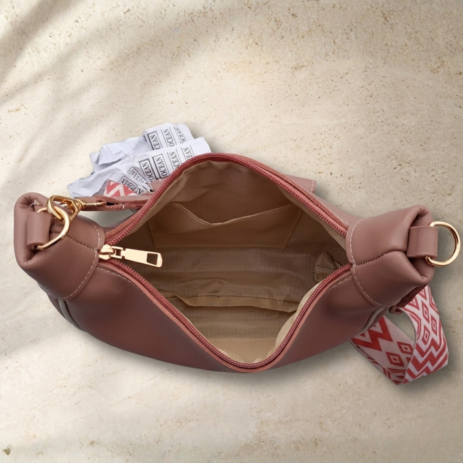 Brown leather handbag with a gold zipper on a beige background